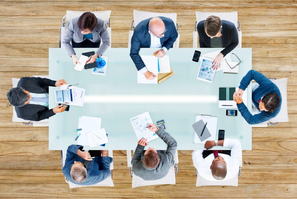 מבט מלמעלה על שולחן ישיבות ואנשים יושבים סביבו עם דפים